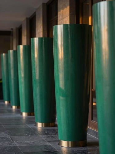 Bespoke emerald green cylindrical planters lining a luxury hotel corridor, soft golden-hour light reflecting on the smooth finish