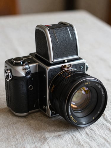 A close-up of a medium-format film camera resting on a raw linen tablecloth, soft side light, grainy texture.
