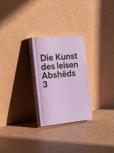 A minimalist book cover titled 'Die Kunst des leisen Abschieds' leaning against a textured terracotta plaster wall, warm golden hour sunlight, soft lavender shadows.