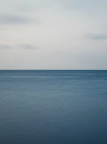 A minimalist landscape featuring a Steel Blue horizon where the sea meets a Pale Grey sky, captured with a long exposure for a smooth, immersive texture.
