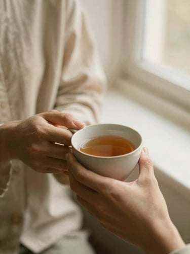 Hands holding a warm ceramic cup of tea, soft linen textures, gentle window light, shallow depth of field