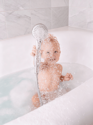 Happy baby playing in a safe clean shower bath after professional repairs in an Auckland home