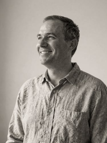 Quiet black and white portrait of a smiling pastor in a simple linen shirt, soft natural side lighting, minimalist background