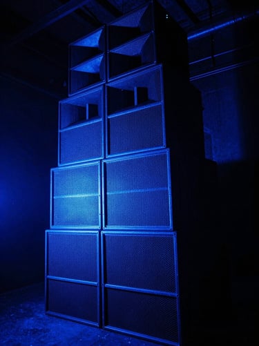 High-contrast strobe lighting illuminating a massive speaker stack in a dark warehouse, saturated neon blue backlighting, deep shadows, gritty texture