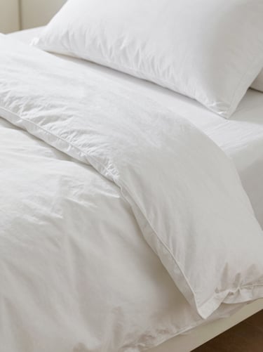 Close-up of double-hemmed organic cotton bedding, crisp white texture, clean minimalist styling, soft natural daylight