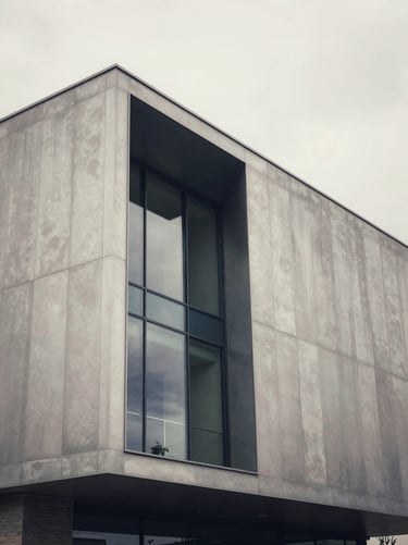 An artistic architectural detail of a contemporary European / French museum exterior. The structure is made of silver grey metal and glass, reflecting a soft off-white sky. The composition is clean, modern, and timeless.