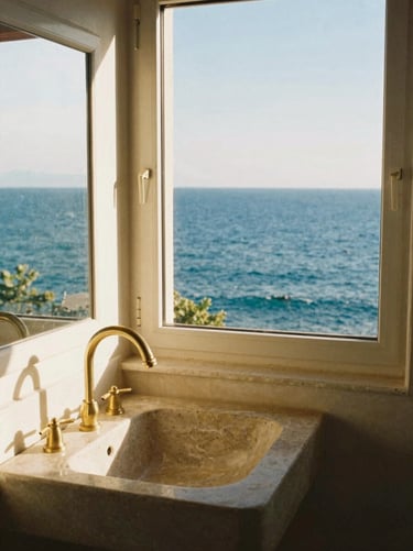 A bright bathroom with a stone sink, brass fixtures, and a window framing the deep blue Adriatic sea
