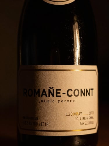 Chiaroscuro macro shot of a Romanée-Conti wine bottle label, dusty glass, low golden light