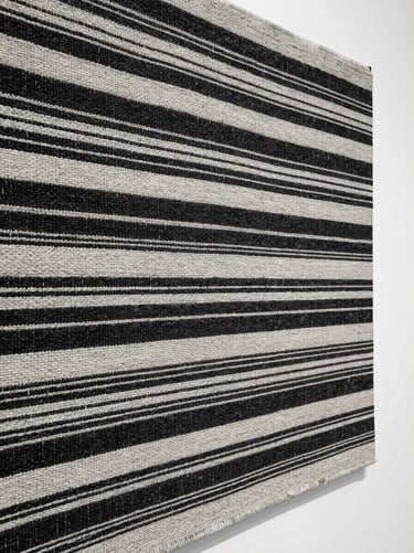 A tight macro shot of hand-woven organic textile art, displaying intricate black and white threads under natural studio light.