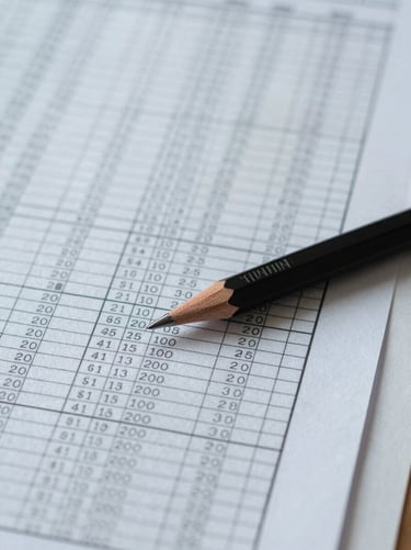 Overhead close-up of a financial spreadsheet and a mechanical pencil resting on ruled paper, cool north-facing daylight, precise analytical work in progress, no people