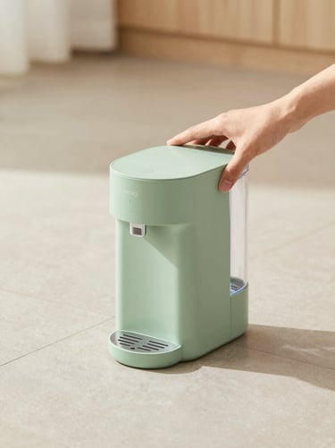 Hands placing a sleek, sage-green pet water dispenser on a clean tiled floor, soft natural daylight, warm neutral tones, crisp focus.