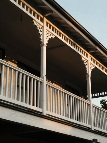 Tight architectural detail of a classic Brisbane Queenslander veranda, deep shadows under timber railings, warm golden hour light reflecting off white painted wood.