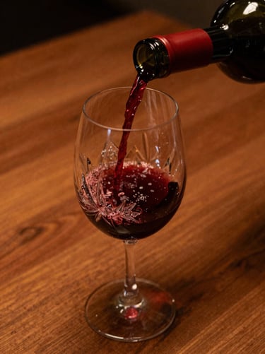 Warm editorial close-up of deep red wine being poured into a crystal glass, rich wood table background, soft ambient lighting, 35mm