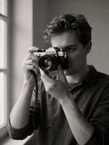 Grainy black and white portrait of a male filmmaker holding a classic rangefinder camera, soft window light, deep charcoal shadows, 35mm film