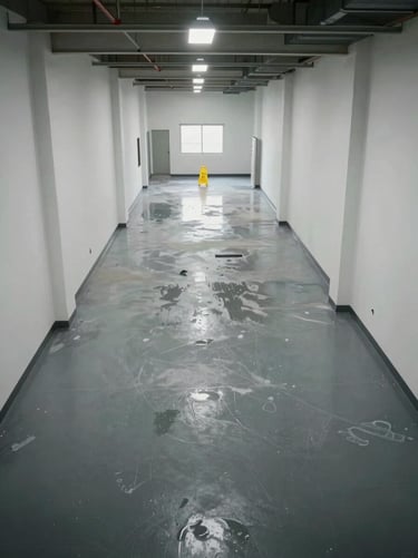 Overhead wide shot of a facility interior — a large empty corridor freshly cleaned, wet-floor signage visible at one end, industrial lighting casting clean shadows, no personnel, post-service completion