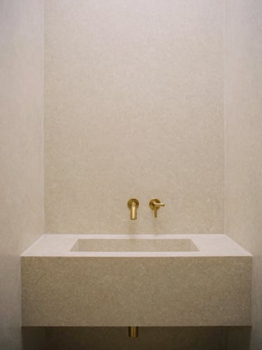 Museum-grade bathroom carved from raw travertine, minimalist brass fixtures, soft diffused daylight