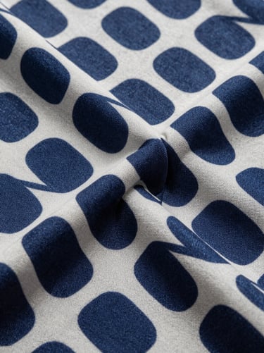 Tight crop of folded polyester fabric bolt showing a seamless geometric print in deep indigo and off-white, studio strobe light revealing print sharpness and weave texture, overhead angle, no styling props
