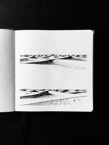 Monochrome flat-lay of an open travel journal with ink drawings of desert horizons, high-contrast direct daylight, sharp shadows