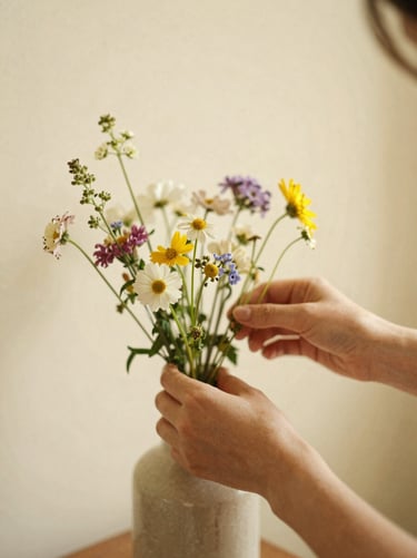 Soft focus photo of hands arranging wild flowers in a ceramic vase, warm natural light