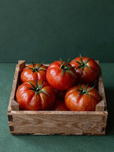 Overhead view of raw organic heirloom tomatoes in a rustic wooden crate, deep forest green background, natural morning light.