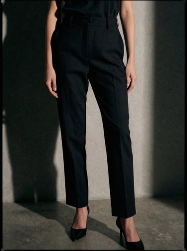 Editorial crop of tailored black trousers on a model, architectural background with clean lines, high-contrast shadows, 35mm film grain.