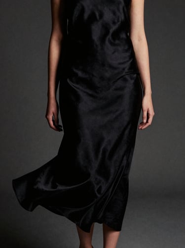 Editorial close-up of a model in a flowing black silk dress, off-center composition, soft moody low-key studio lighting, focus on fabric texture, 35mm film grain.