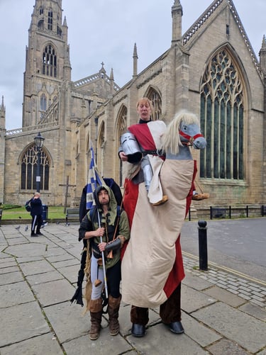Medieval knight on a hobby horse with his squire standing in front of a historic gothic cathedral.