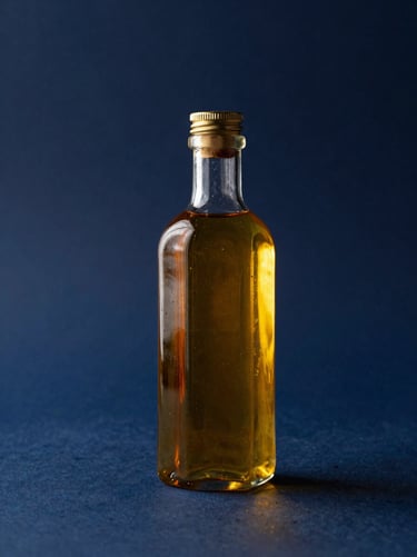 A refined glass bottle containing clear golden anointing oil, reflecting warm dramatic stage lighting against a deep navy background