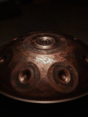 Intimate close-up of a steel handpan reflecting soft studio light, deep shadows, moody dark tones, 35mm film grain