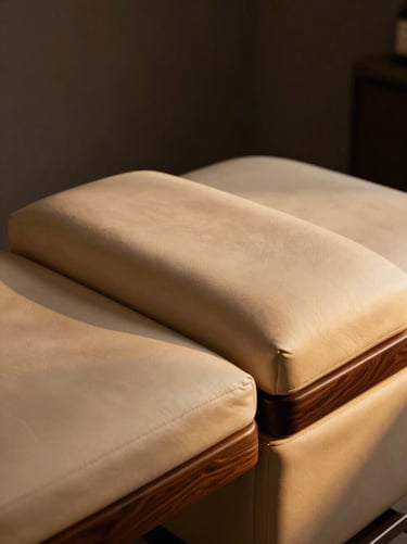 Close-up of a luxury facial and massage bed, rich cream leather upholstery, dark wood accents, soft warm lighting
