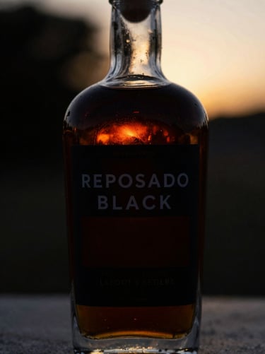 Macro shot of a dark glass tequila bottle labelled Reposado Black, dark mysterious amber liquid, dramatic low-key lighting, black background.