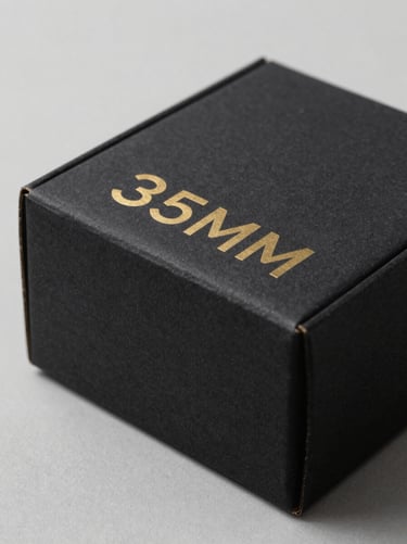 Minimalist matte black cardboard packaging box with gold foil lettering, soft diffused lighting, 35mm