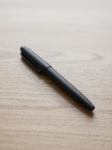A minimalist matte black fountain pen resting on raw oak wood, soft overhead daylight