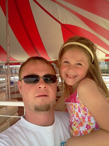 Man wearing dark sunglasses and child are posing under a red and white striped canopy