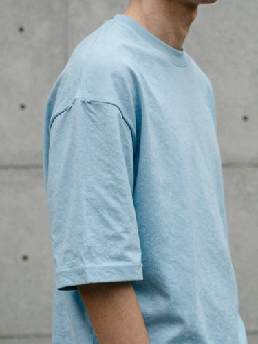 Close-up texture shot of a model wearing an oversized ice-blue t-shirt, focused on the drop-shoulder seam, urban concrete background.