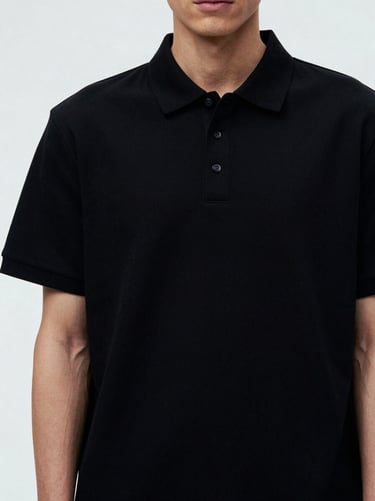 Medium shot of a model wearing a heavyweight black polo t-shirt, structured collar visible, minimal studio setting.