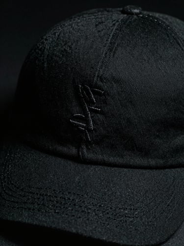 Extreme close-up of a black cotton cap with subtle matte embroidery, dramatic side lighting, 35mm film texture.