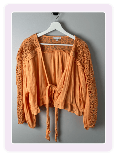 American Eagle orange long-sleeve tie-front crop top with boho lace detail hanging on a white hanger.