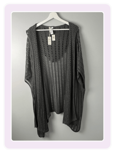 Charcoal gray open front crochet knit cardigan wrap hanging on a white hanger against a gray wall.