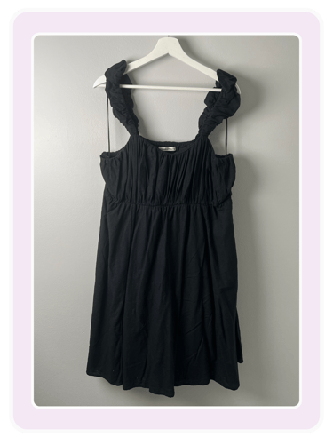 Black sleeveless mini dress with ruffled straps and a gathered bodice hanging on a white hanger.
