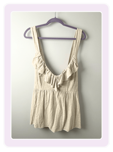 Beige linen ruffled tank top with deep v-neck hanging on a purple hanger against a white wall.