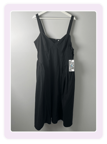 A black sleeveless midi dress by Future Collective hanging on a white hanger against a gray wall.