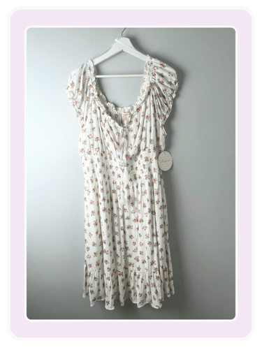White cottagecore dress with pink floral print, ruffled sleeves, and smocked waist on a hanger.