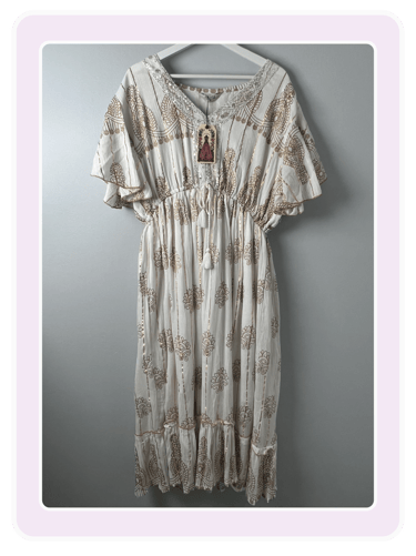 White boho maxi dress with gold floral print and lace V-neck hanging on a hanger.