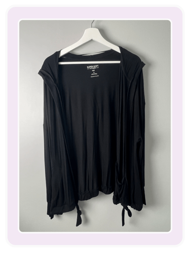 Super soft black open-front cardigan with a hood hanging on a white wooden hanger against a gray wall.