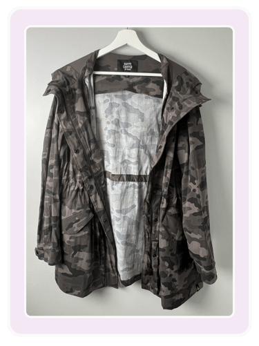 Happy Camper by Torrid camouflage hooded parka jacket hanging on a white hanger against a gray wall.