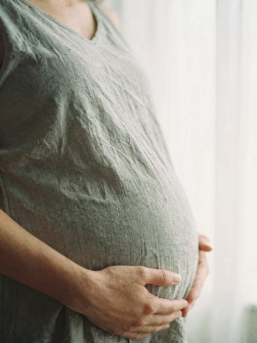 Gentle hands-on-belly shot of an expectant mother, warm morning window light, soft linen textures, shallow depth of field, 35mm film.