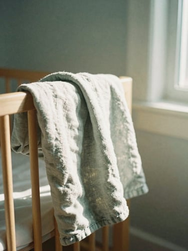 A quiet, sunlit nursery corner with a soft linen blanket draped over a wooden chair, natural window shadows, shallow depth of field, 35mm film.