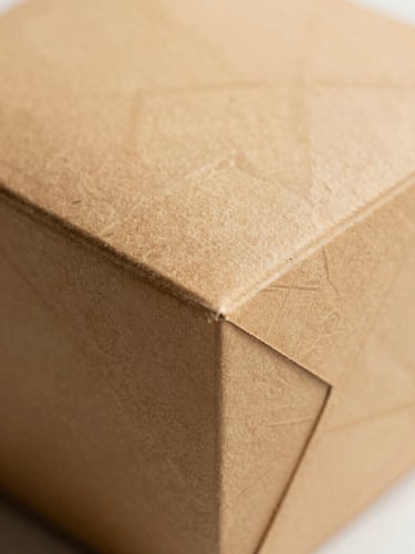 Macro shot of heavy-milled paper texture on a structured sweet box, minimalist South Asian geometric pattern, soft warm lighting.
