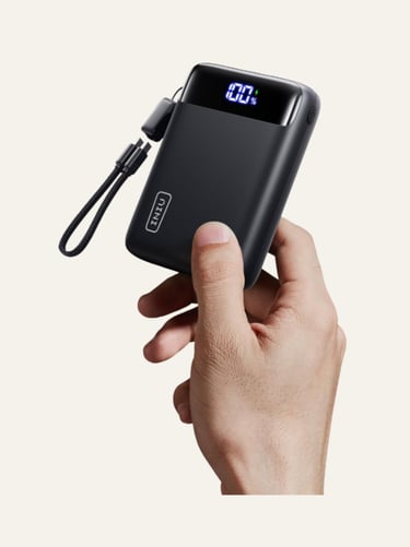 Hand holding a compact black INIU portable charger with a digital LED display showing 100 percent battery life.